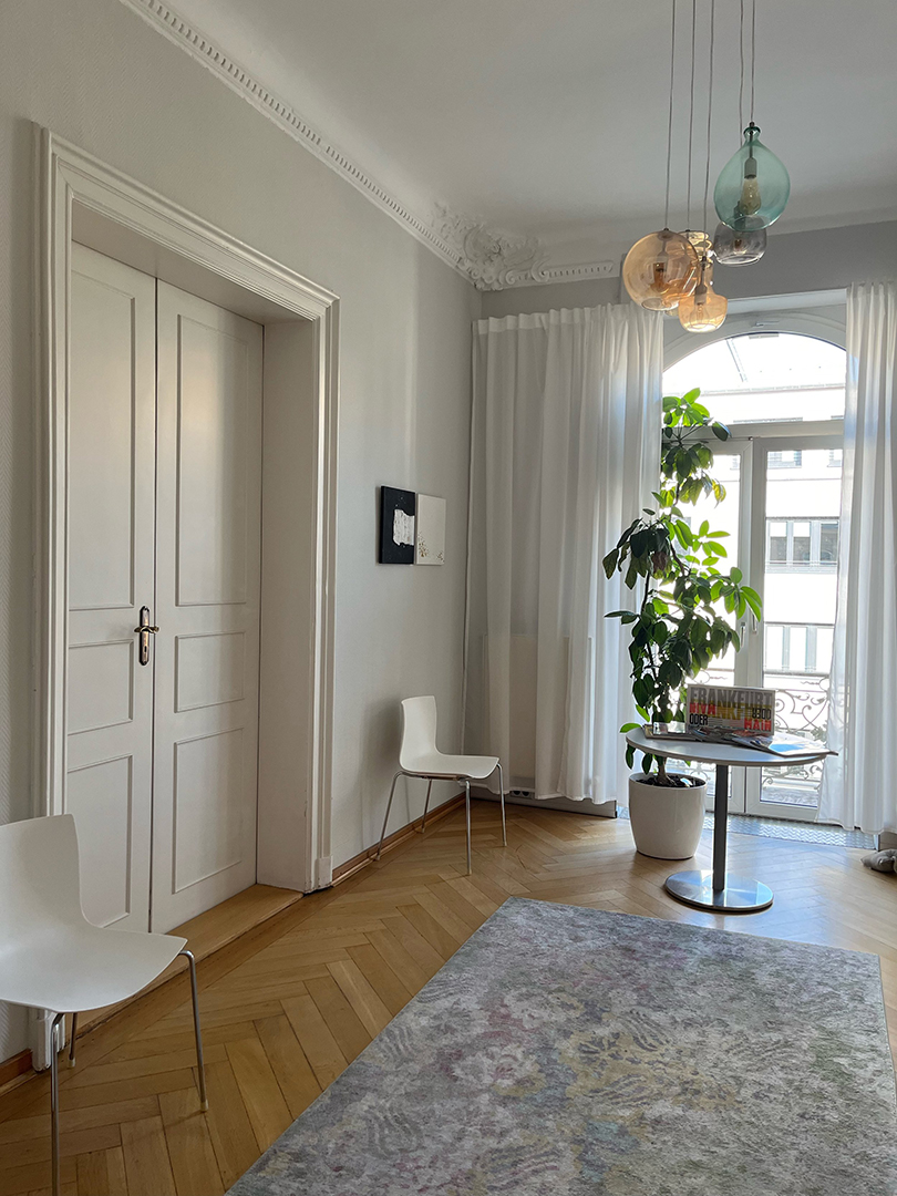 wartebereich_810x1080 Wartebereich der Privatpraxis für Psychotherapie: ein heller Raum in einem stilvollen Altbau mit Stuckdecken, Holzparkett und weißen, modernen Möbeln.